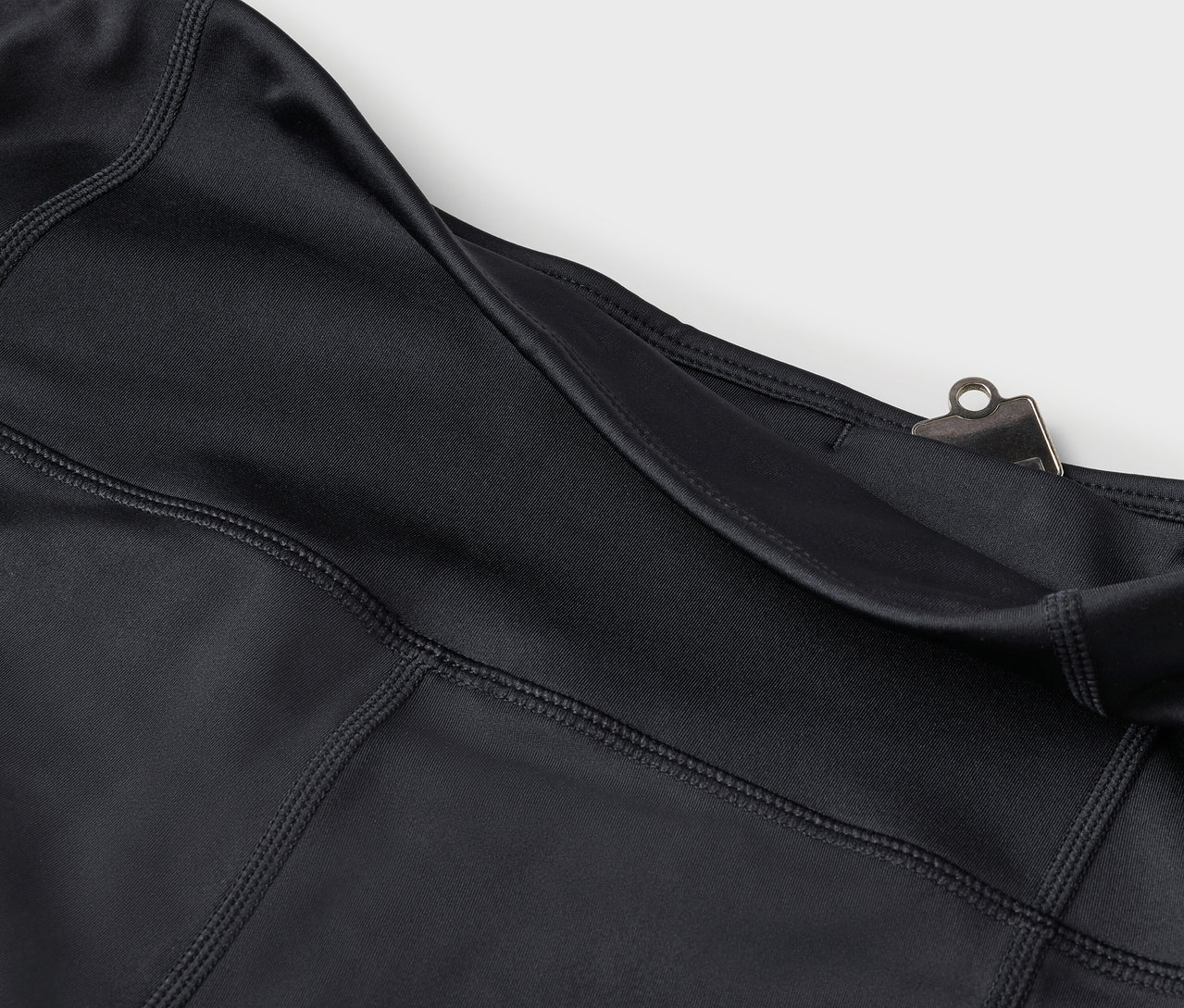 Détail de leggings noirs avec poche et clip argenté.