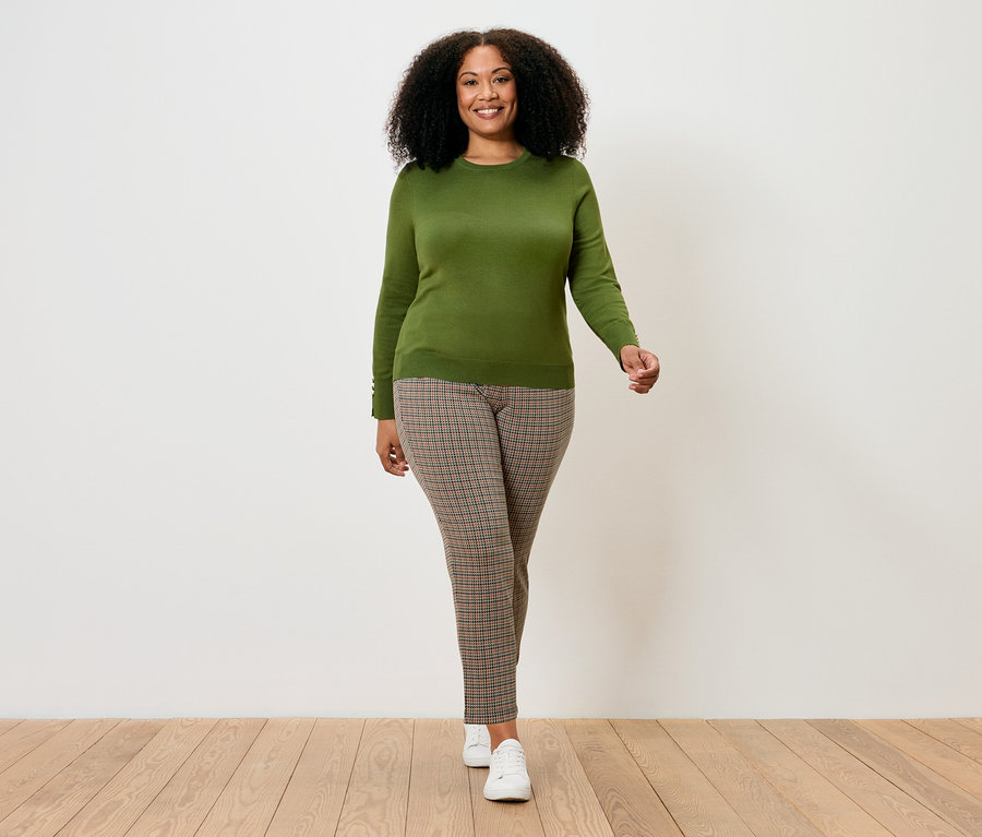 Une femme marche et porte un pull en maille fine vert clair.