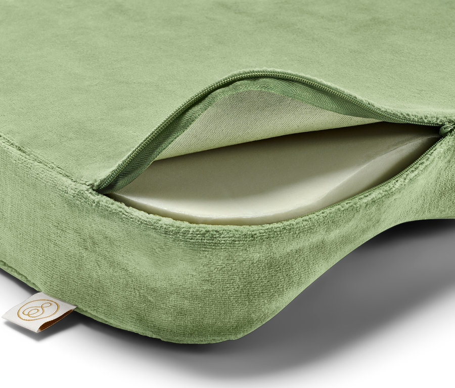 Coussin vert avec une fermeture éclair révélant l'intérieur blanc et une étiquette dans le coin inférieur gauche.
