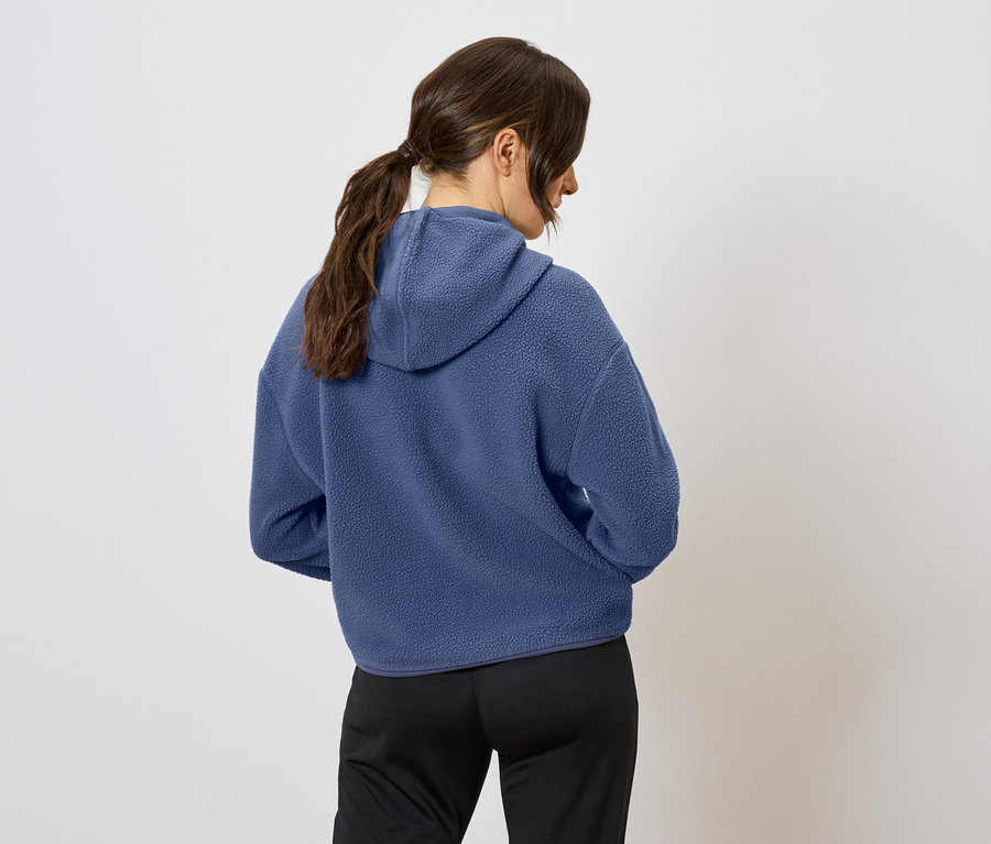 Vue arrière d'une femme aux cheveux bruns attachés en queue de cheval, portant un sweat à capuche bleu et un pantalon noir.