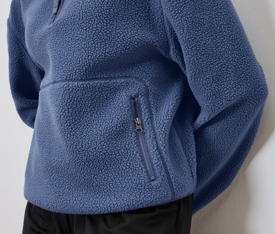Gros plan sur un pull en polaire bleu avec une poche zippée.