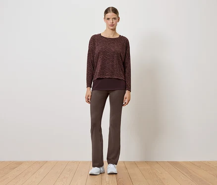 Une femme portant un pull marron et un pantalon marron se tient sur un plancher en bois.