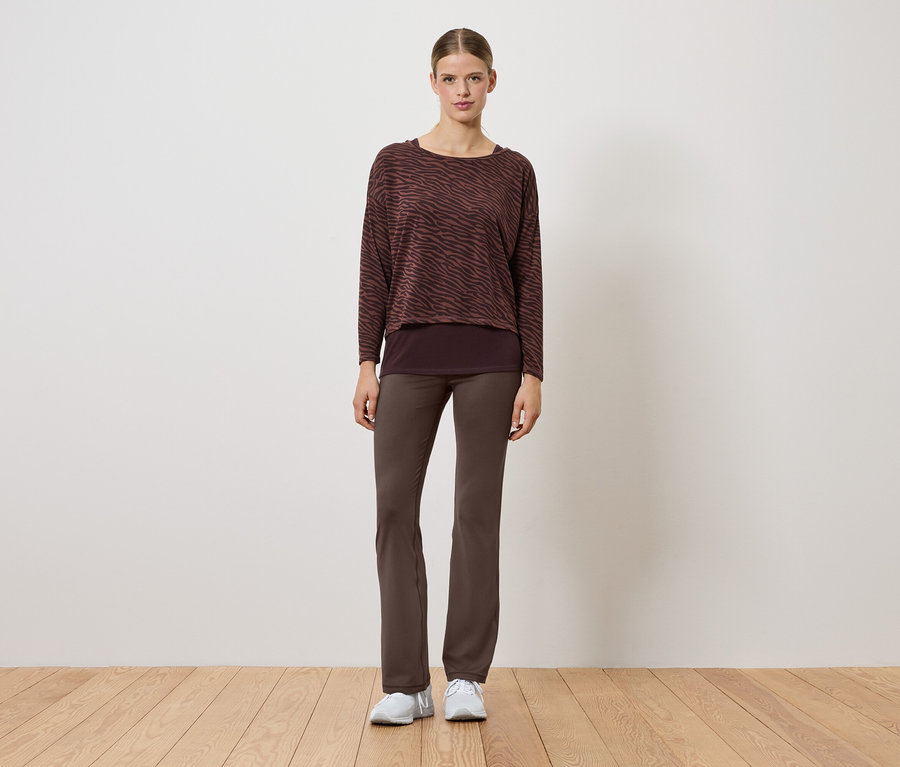 Une femme portant un pull marron et un pantalon marron se tient sur un plancher en bois.