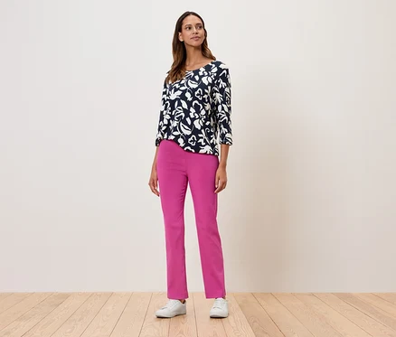 Une femme debout portant un haut à fleurs à manches trois-quarts, un pantalon rose et des baskets blanches.