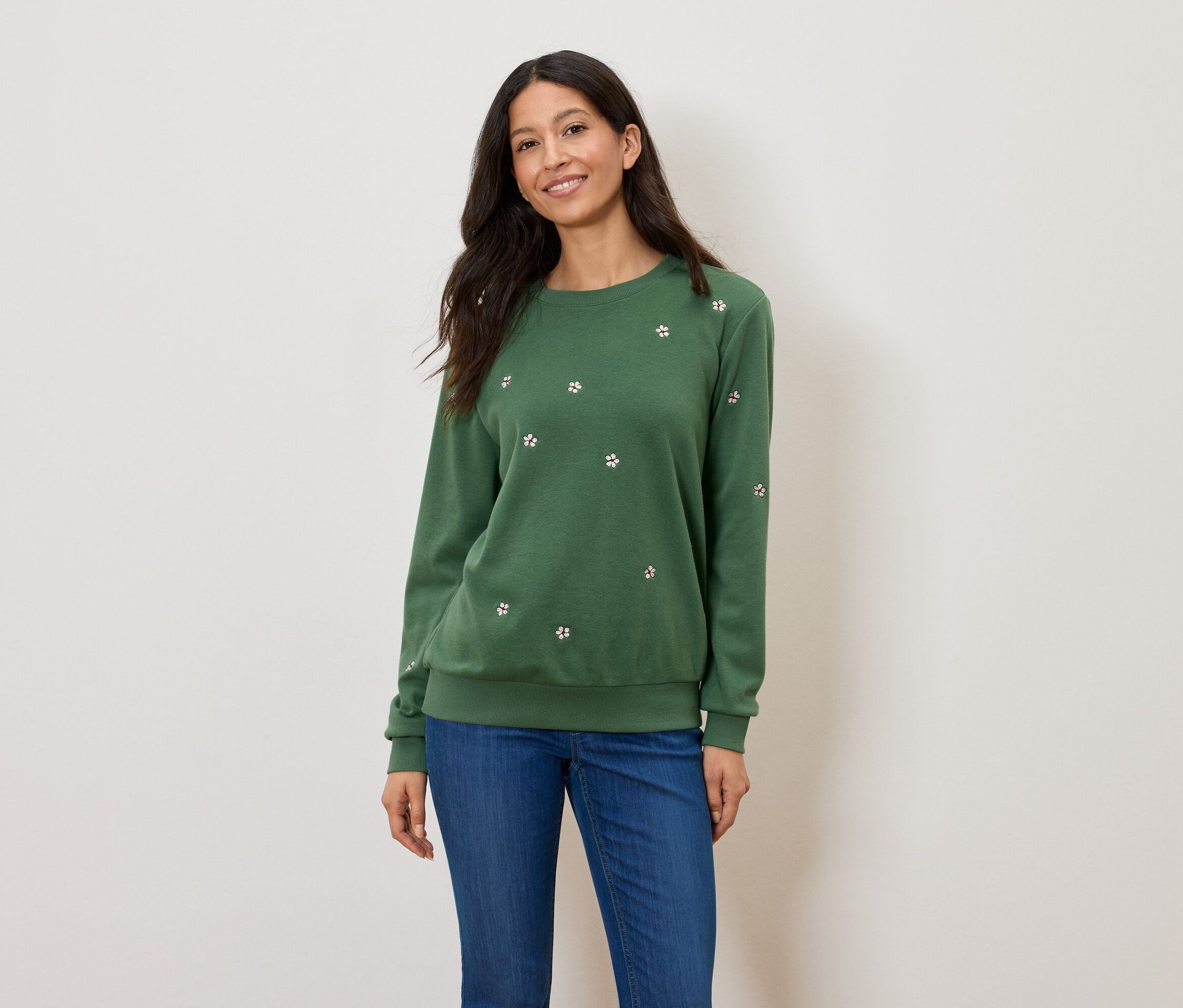 Femme portant un pull vert à motifs floraux et un jean bleu.