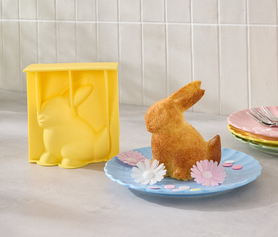 Un moule à gâteau en forme de lapin jaune est à côté d'un lapin cuit sur une assiette bleue avec des fleurs.