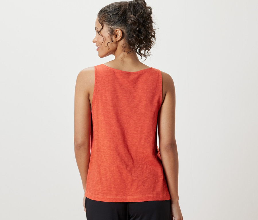 Une femme porte un haut orange en mélange modal et un pantalon noir.