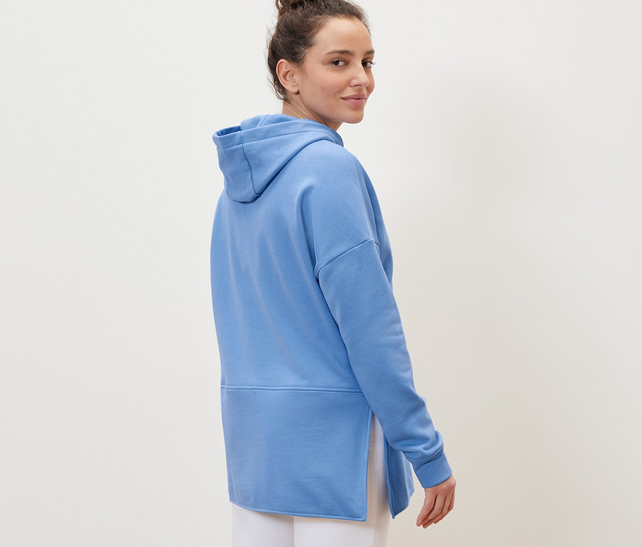 Femme regardant par-dessus son épaule portant un sweatshirt long à capuche bleu clair.
