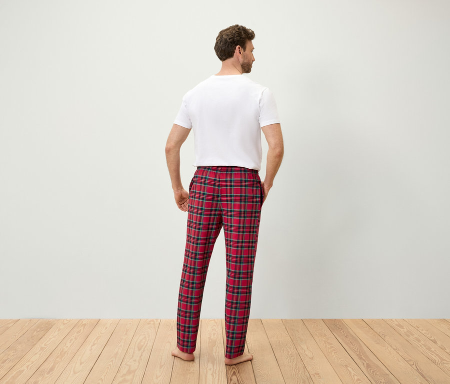 Un homme, vu de dos, les mains dans les poches d'un pantalon de pyjama à carreaux rouges, portant un t-shirt blanc.
