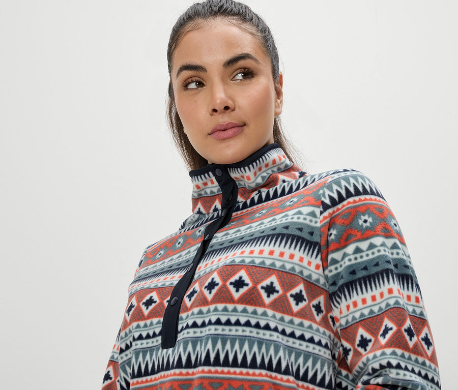 Portrait d'une femme aux cheveux bruns portant un haut en polaire multicolore à motif géométrique.
