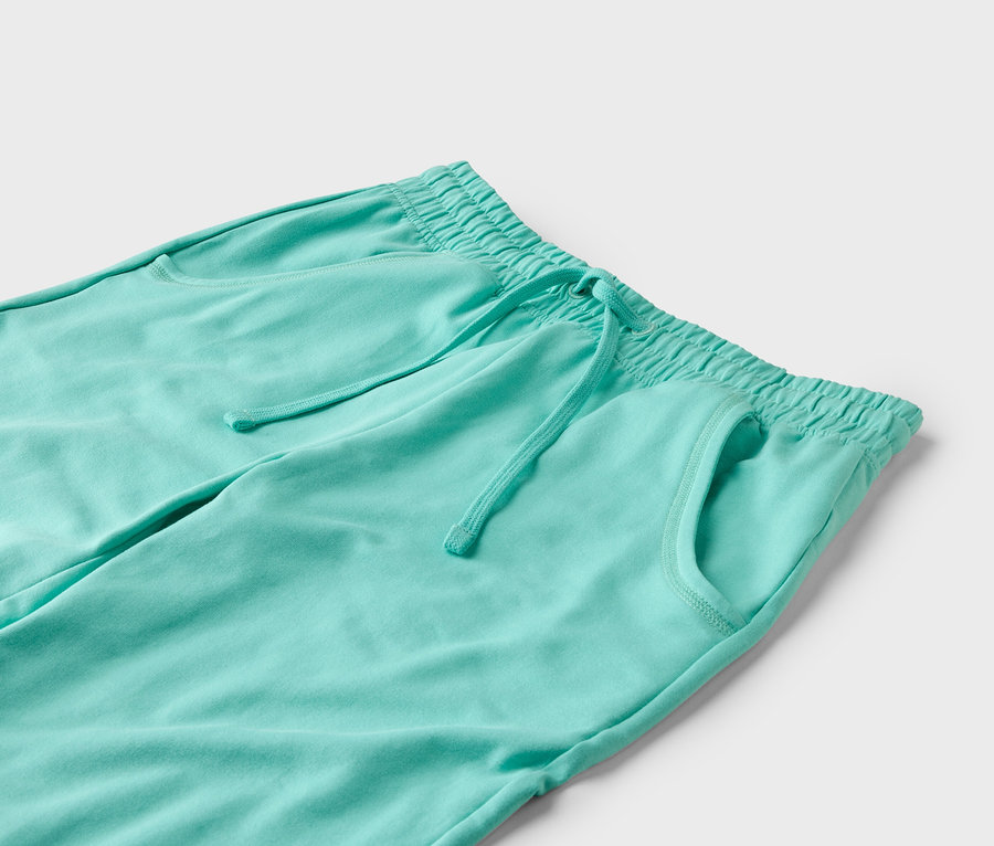 Gros plan d'un pantalon de jogging turquoise avec cordon de serrage et poches sur fond blanc.