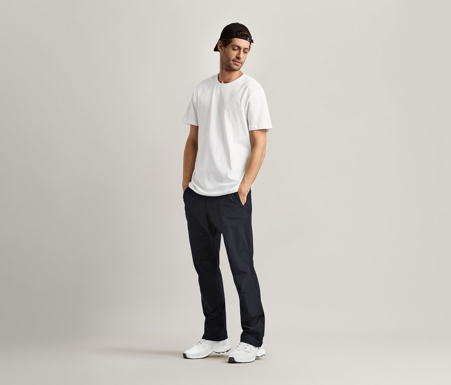 Un homme se tient debout, les mains dans les poches, et porte 2 T-shirts à encolure ronde, blanc.