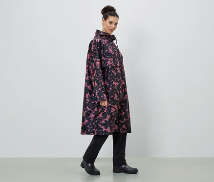 Une femme porte un long imperméable à fleurs rose et noir, avec un pantalon et des bottes noirs.