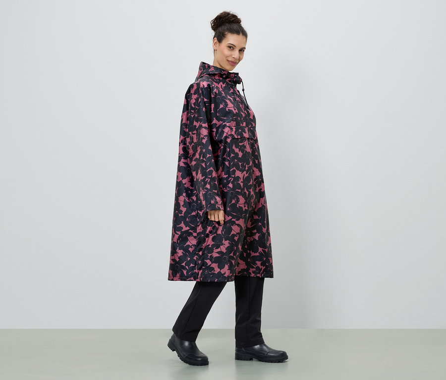Une femme porte un long imperméable à fleurs rose et noir, avec un pantalon et des bottes noirs.