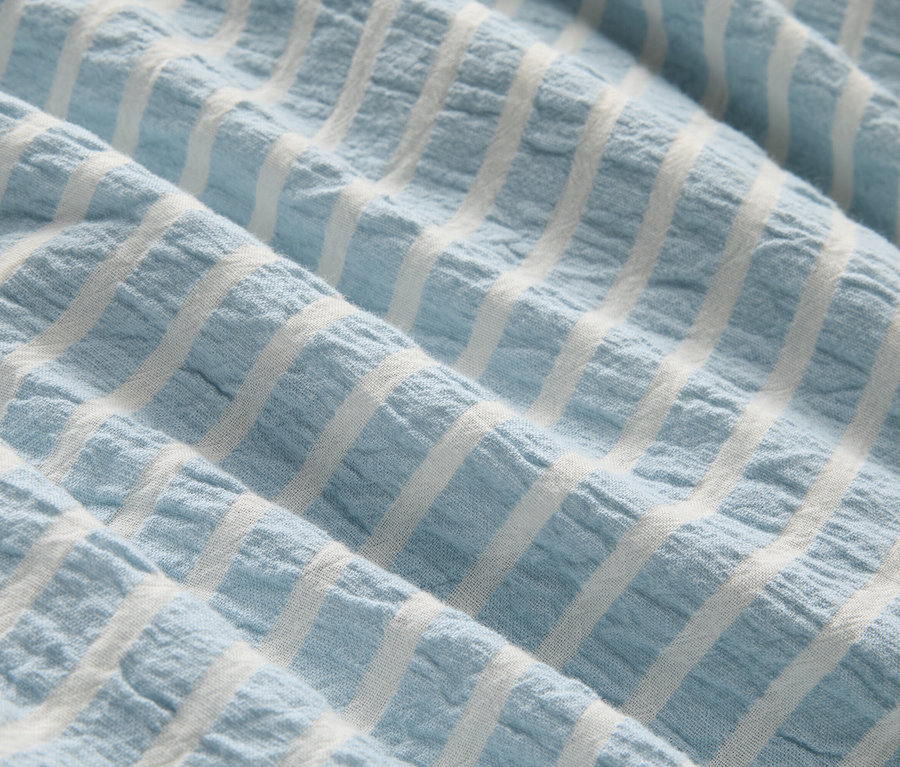Gros plan d'un tissu bleu clair à rayures blanches avec des plis.