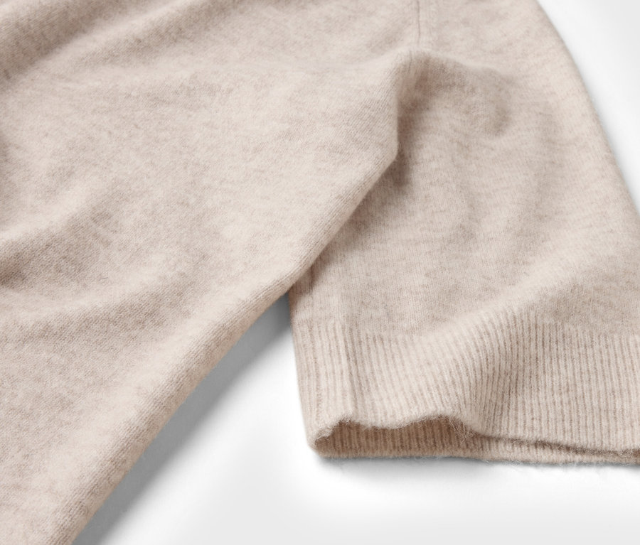 Gros plan d'un pull en tricot beige à manches courtes sur fond blanc.