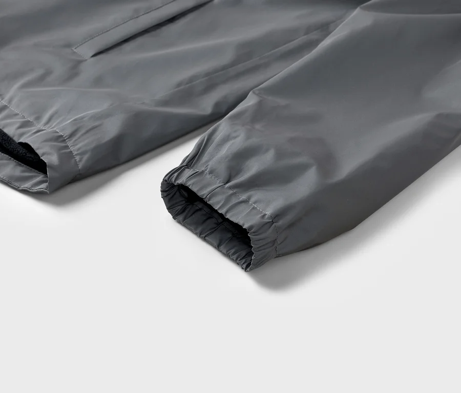 Gros plan sur la manche grise d'une veste avec un poignet élastique sur fond blanc.