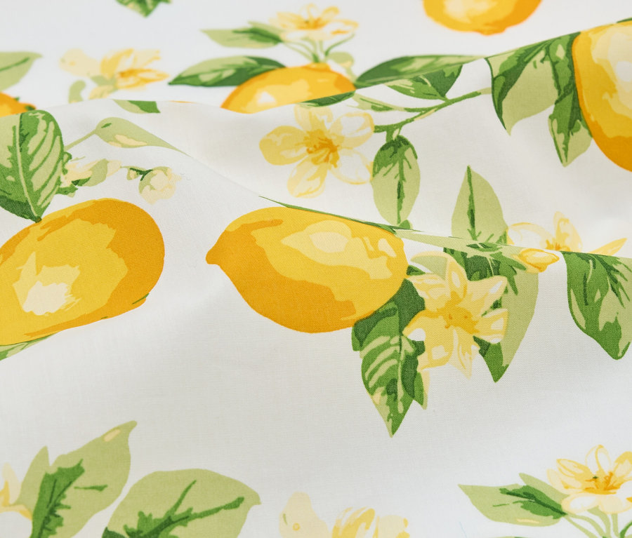 Gros plan d'un tissu blanc avec des citrons, des feuilles et des fleurs jaunes.