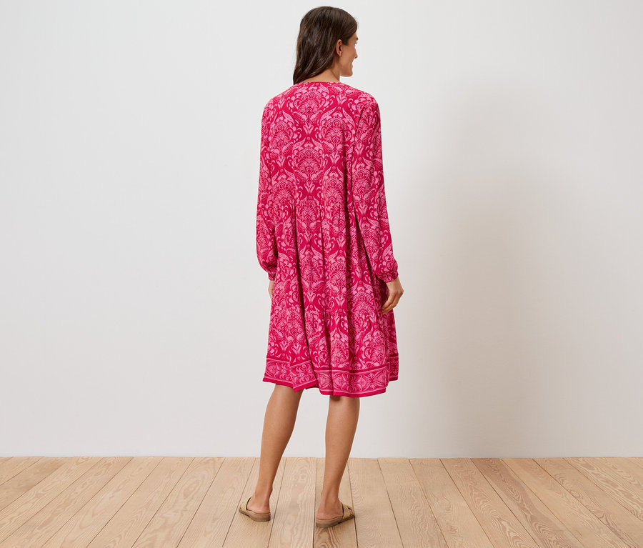 Vue de dos d'une femme portant une robe rose à fleurs jusqu'aux genoux et des sandales.