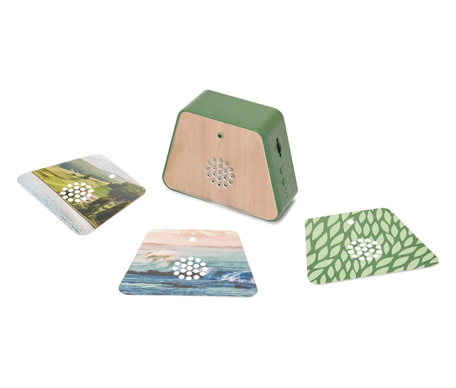 Un haut-parleur vert avec des détails en bois se trouve sur une surface blanche, entouré de trois cartes carrées avec des motifs de paysage.