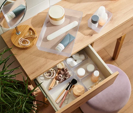 Coiffeuse avec tiroir ouvert et divers produits cosmétiques, notamment des crèmes, des tubes et des accessoires de maquillage.