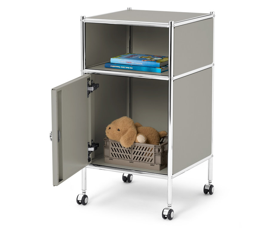 Un meuble de rangement gris sur roulettes avec un compartiment ouvert sur le dessus avec deux livres et un compartiment ouvert sur le dessous avec un ours en peluche dans une caisse grise.