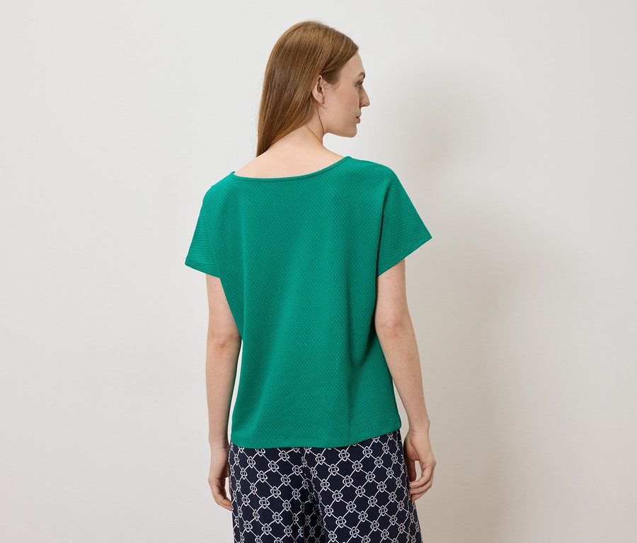 Femme vue de dos, portant un haut court vert et un pantalon foncé à motifs.