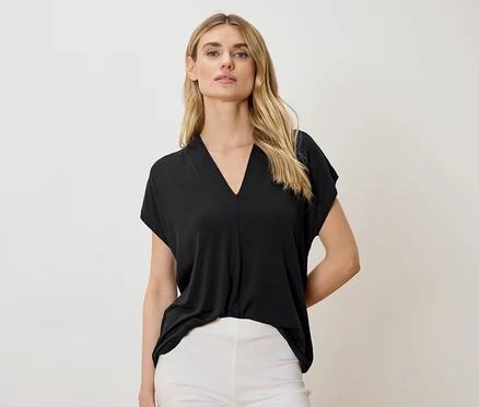 Une femme porte un haut noir à col en V et un pantalon blanc.