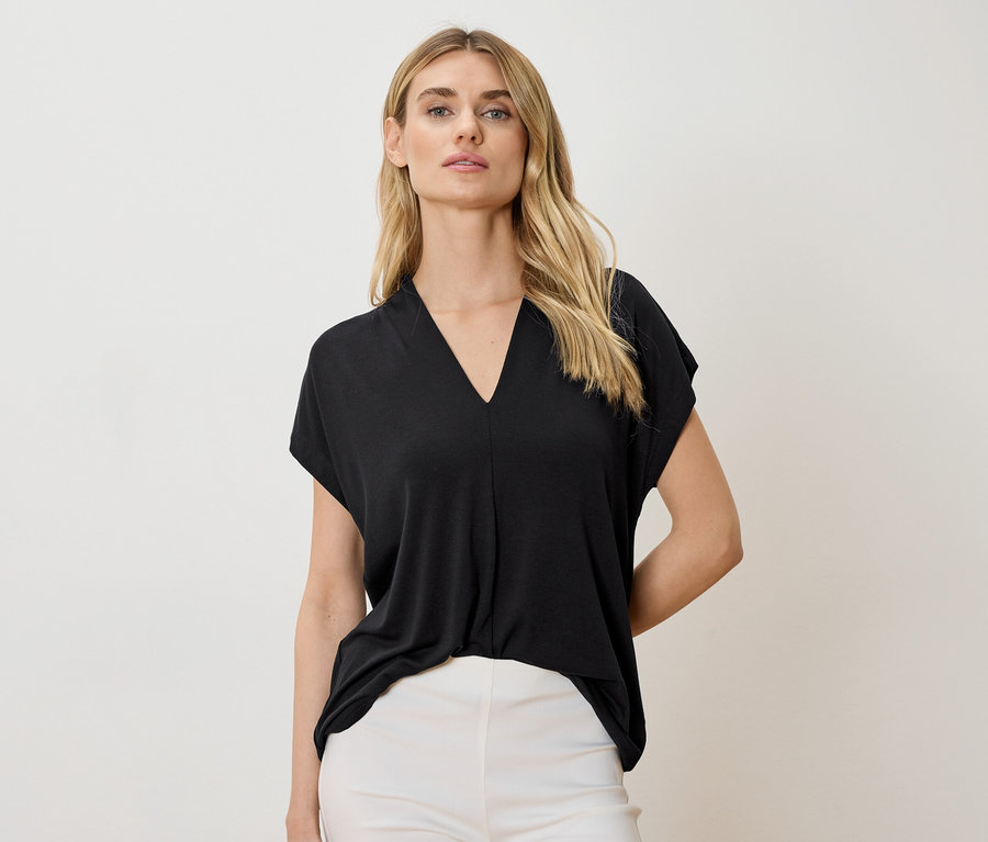 Une femme porte un haut noir à col en V et un pantalon blanc.