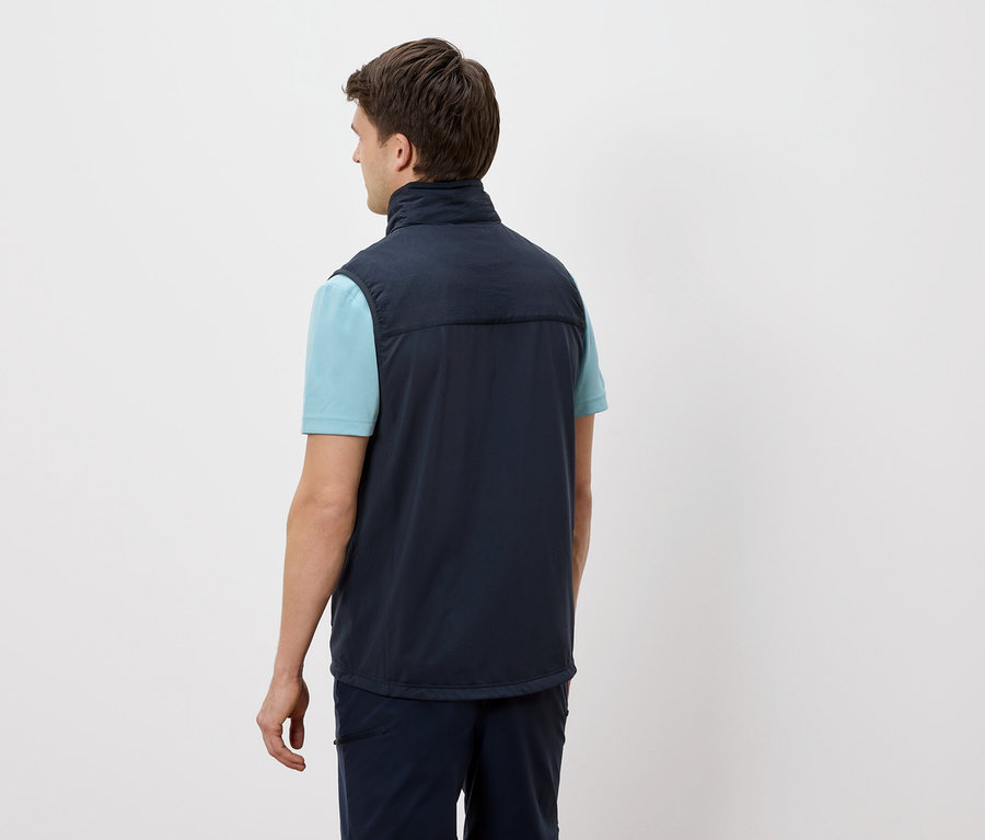 Un homme se tient dos à la caméra, portant un gilet bleu marine sur un t-shirt bleu clair.