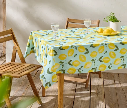 Une table avec une nappe citron bleu clair, deux verres, des citrons sur une assiette et une plante en pot.