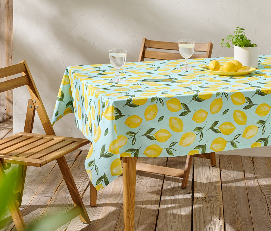 Une table avec une nappe citron bleu clair, deux verres, des citrons sur une assiette et une plante en pot.