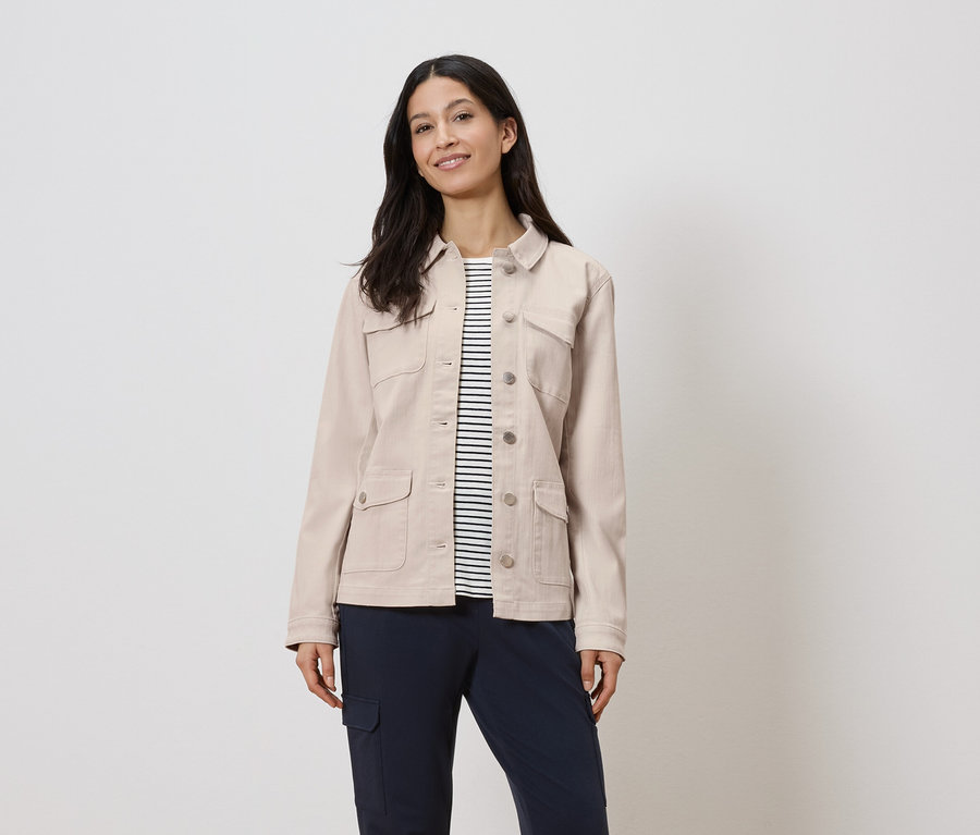 Une femme porte une veste beige sur une chemise rayée et un pantalon bleu marine.