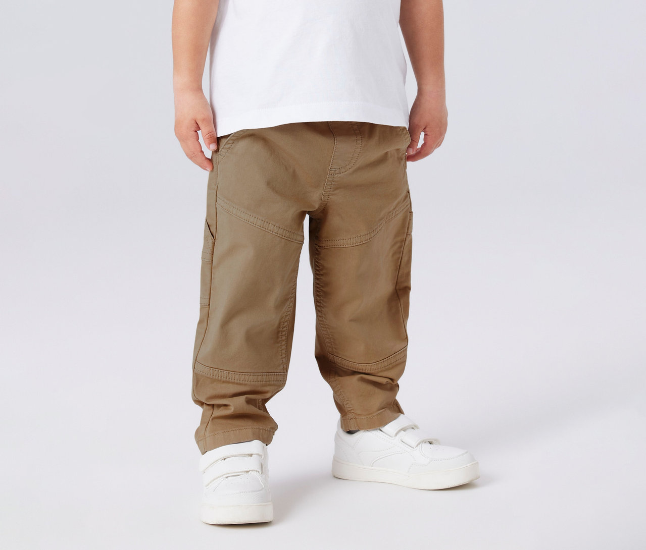 Un enfant porte un t-shirt blanc, un pantalon en sergé pour enfant NAME IT et des baskets blanches.