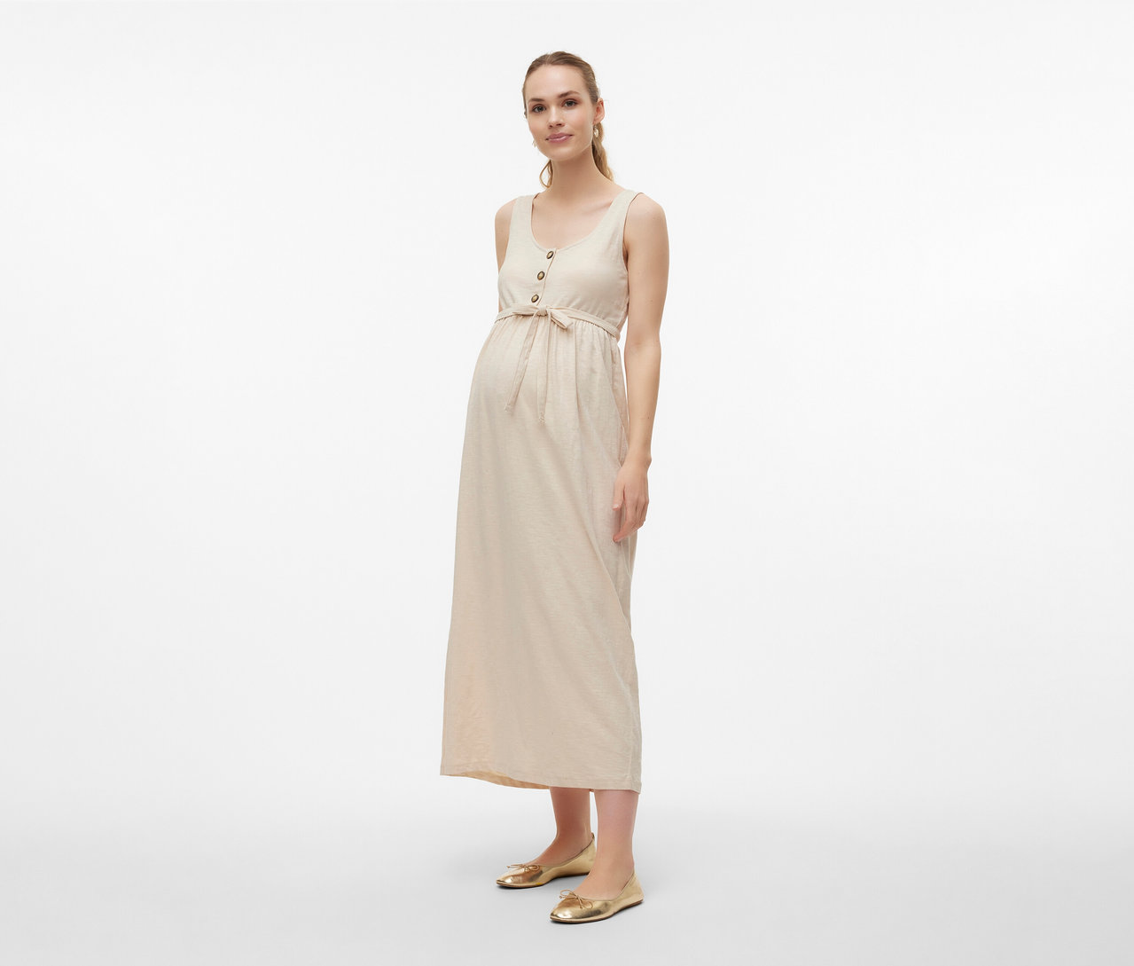 Femme portant une robe de grossesse MAMALICIOUS «
MLEVI LIA » avec ceinture et ballerines dorées sur fond clair.