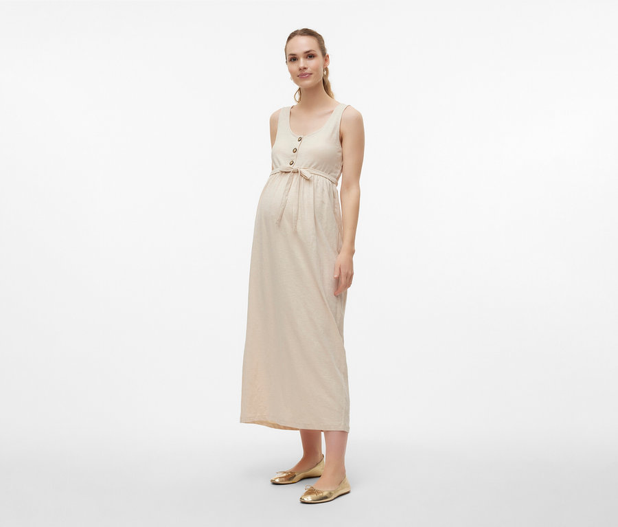 Femme portant une robe de grossesse MAMALICIOUS «
MLEVI LIA » avec ceinture et ballerines dorées sur fond clair.