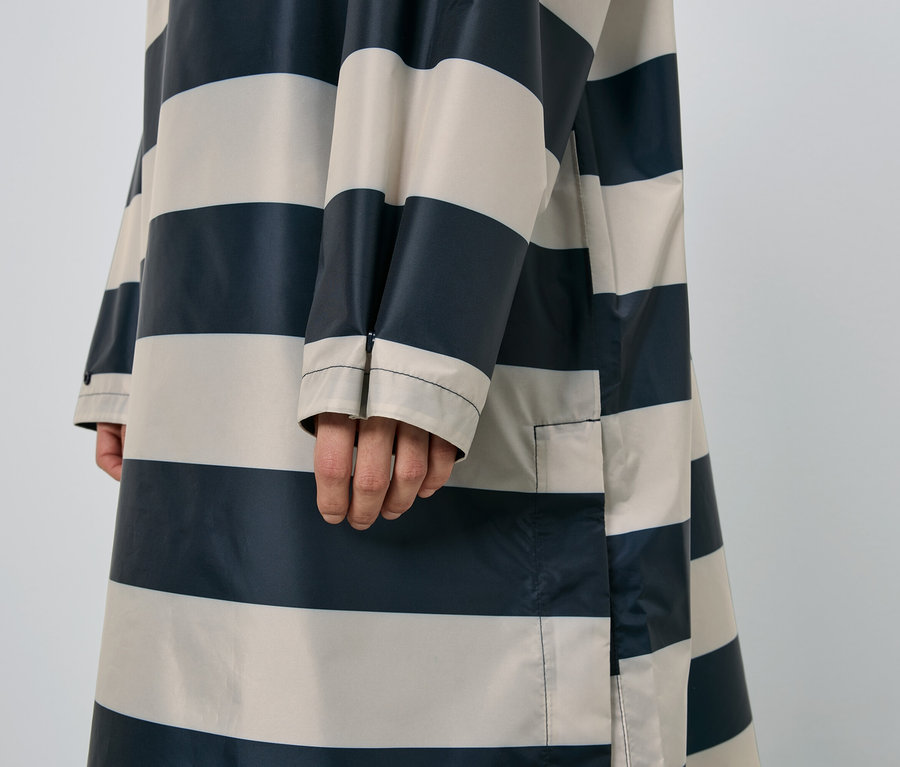 Gros plan d'une personne portant un imperméable rayé bleu marine et beige.