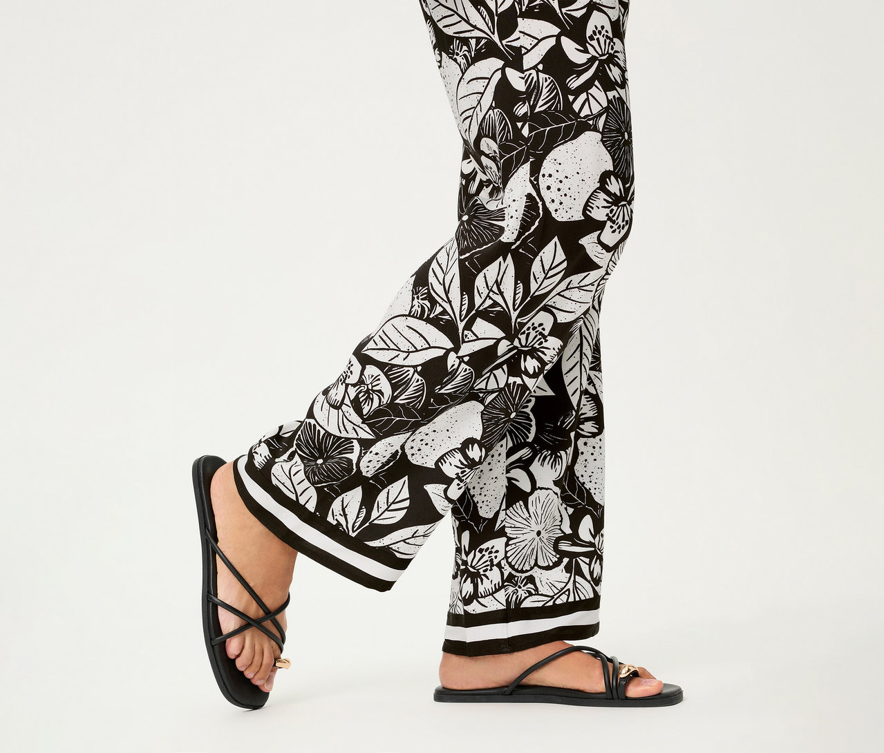 Jambes portant un pantalon large Olsen à motif floral noir et des sandales à lanières.