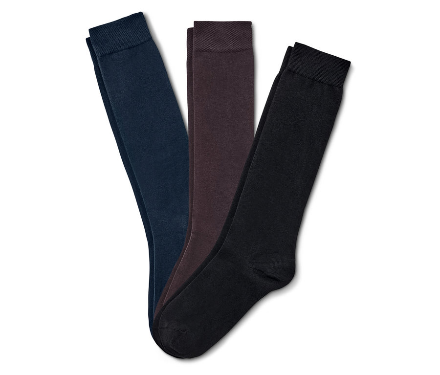 Trois chaussettes pliées bleu marine, marron et noires sont posées sur un fond blanc.