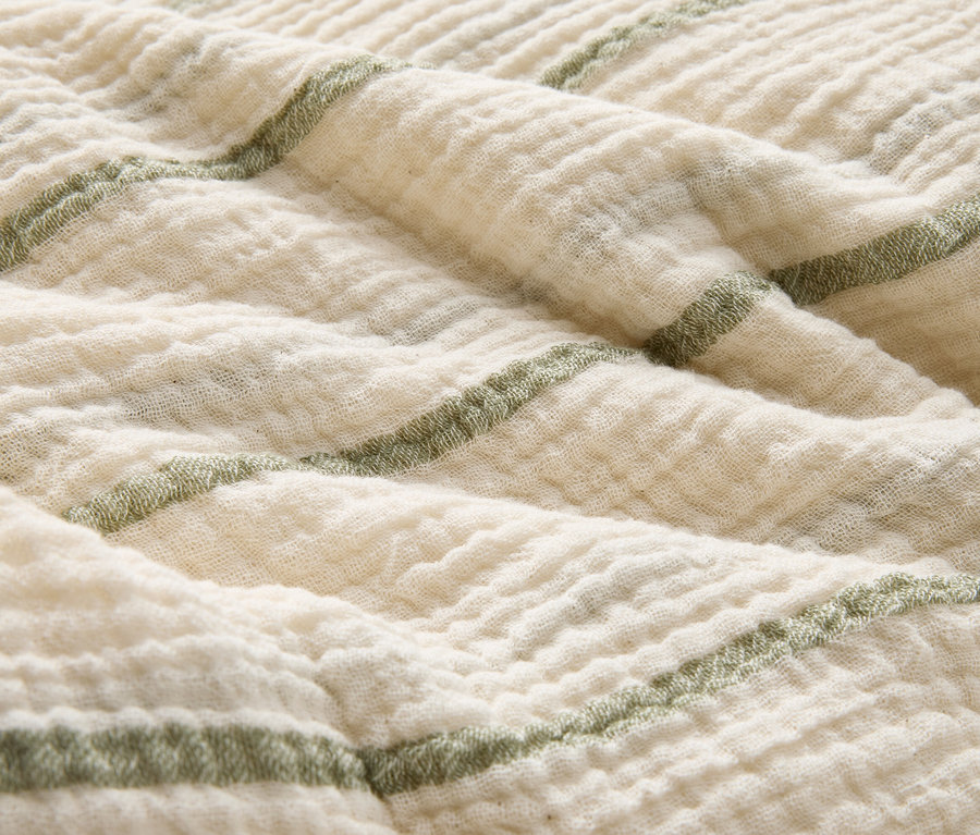 Gros plan d'une couverture en tissu crème pliée avec des rayures vertes.