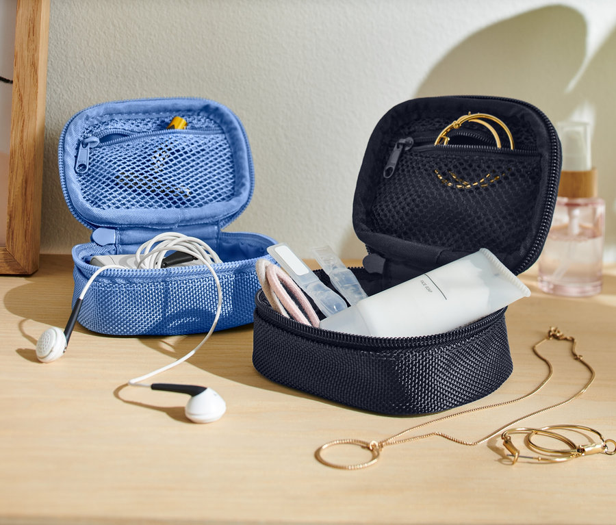 Sur une table, deux petits sacs de rangement ouverts, un bleu avec des écouteurs et un foncé avec des produits de soin et des bijoux.