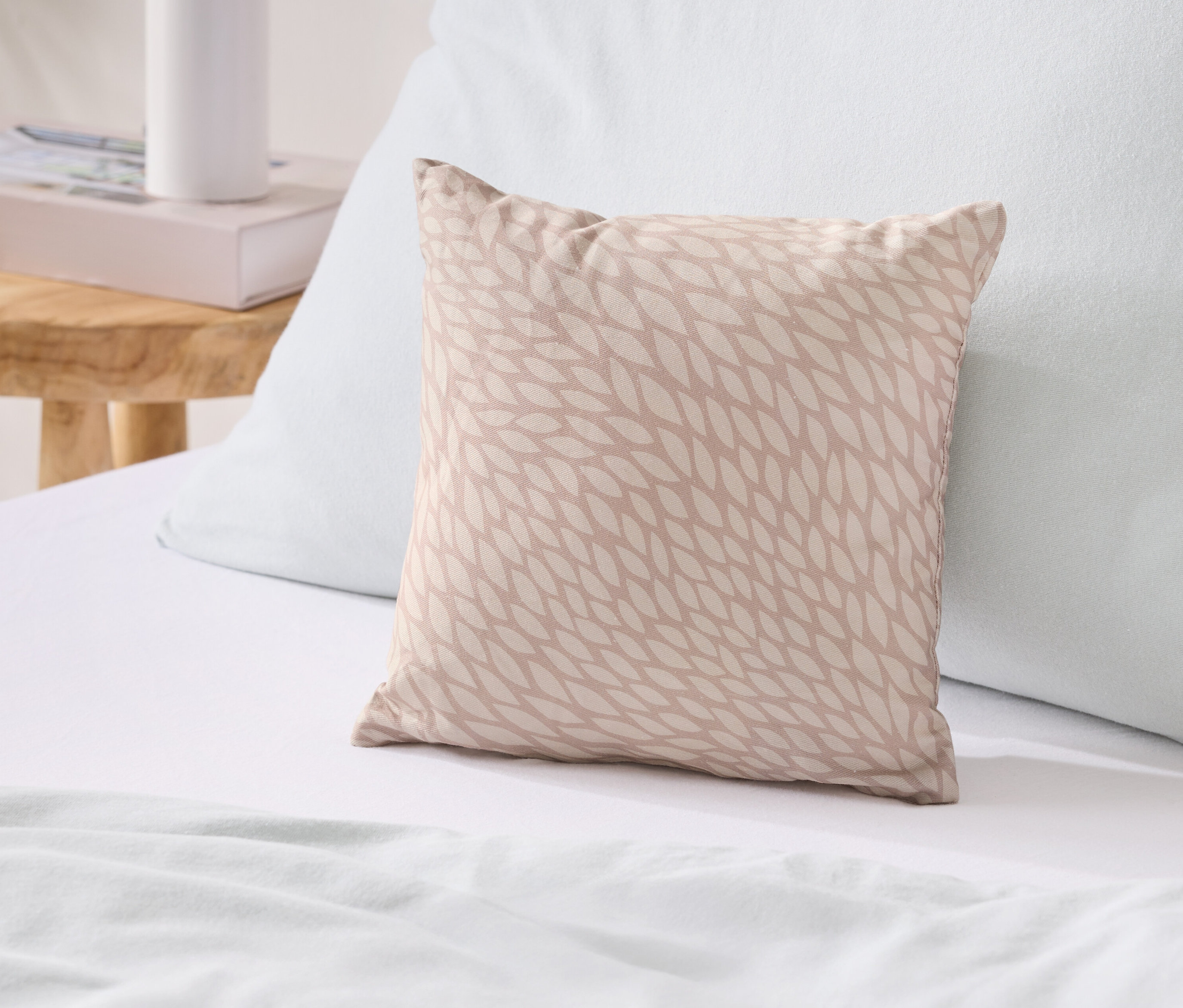 Un coussin beige à motifs de feuilles repose sur un lit à côté d'un coussin bleu.