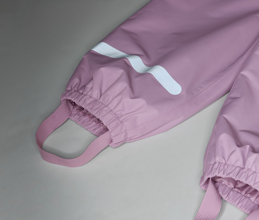 Gros plan sur un pantalon de pluie rose avec des bretelles élastiques et des bandes réfléchissantes sur les jambes.