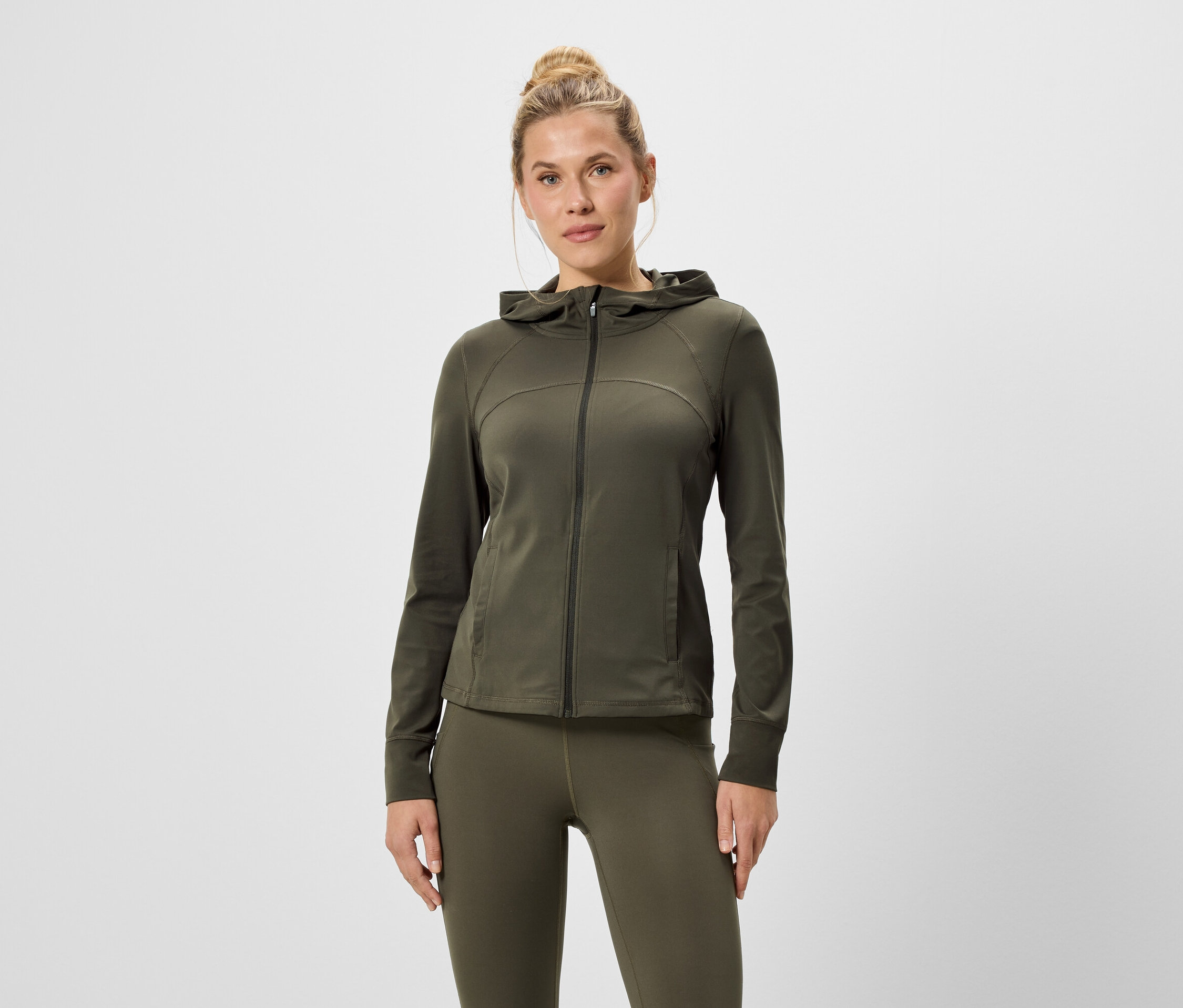 Femme portant un sweat à capuche zippé vert olive et un legging.