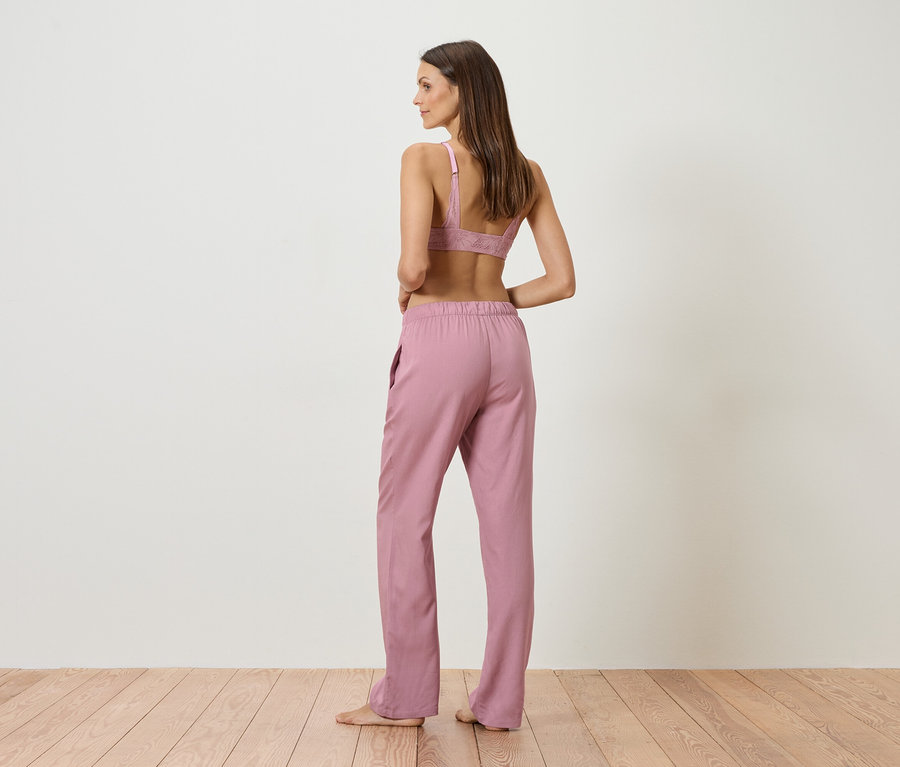 Vue de dos d'une femme aux longs cheveux bruns portant un soutien-gorge rose et un pantalon rose.