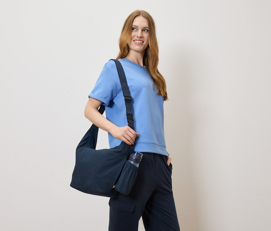 Femme portant un t-shirt bleu et un pantalon bleu, avec un sac bleu sur l'épaule.