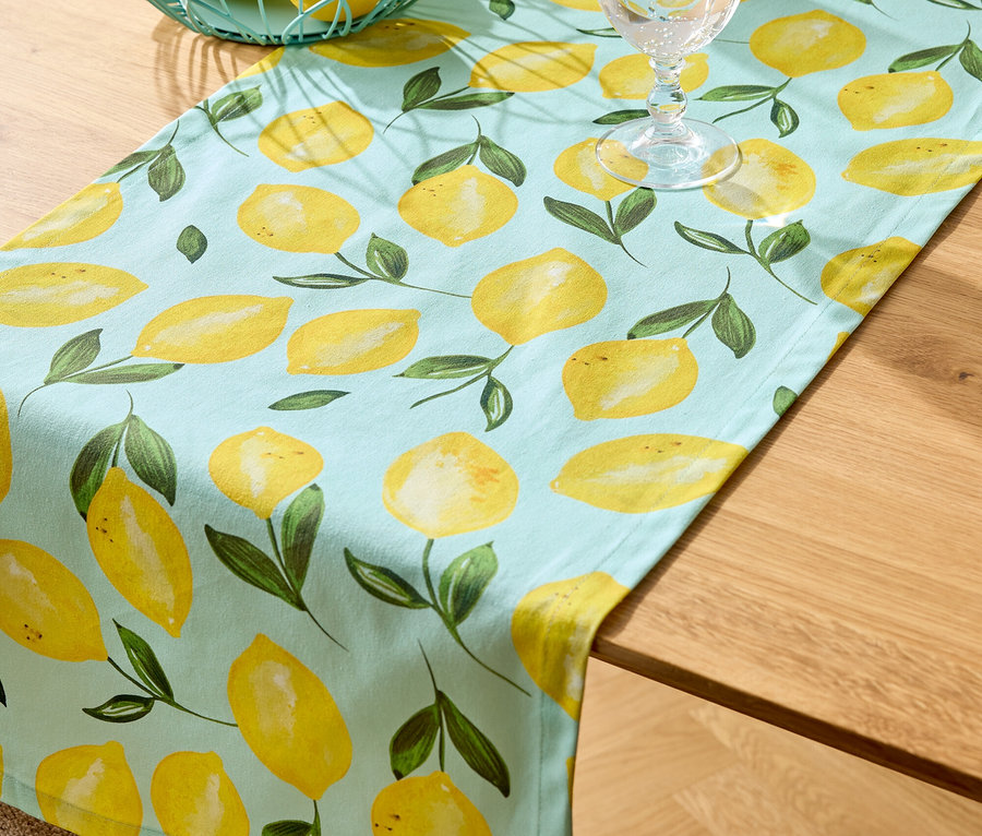 Chemin de table à motif citron, panier en fil de fer avec des citrons, deux verres d'eau sur une table en bois.
