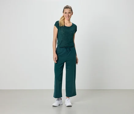 Une femme porte un t-shirt vert, un pantalon vert et des baskets blanches.