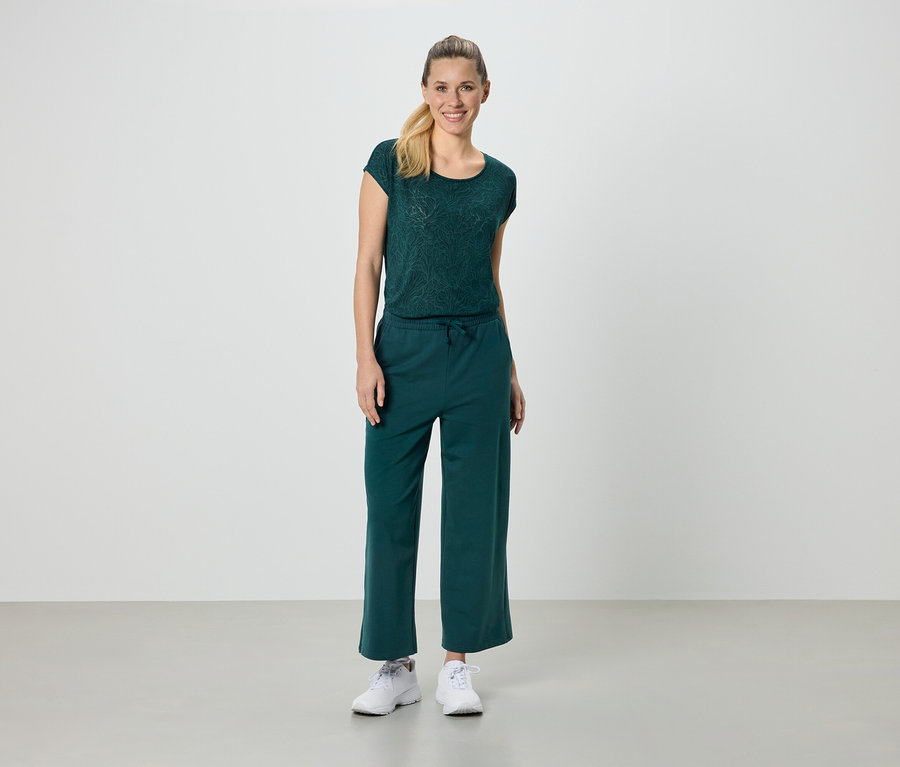 Une femme porte un t-shirt vert, un pantalon vert et des baskets blanches.