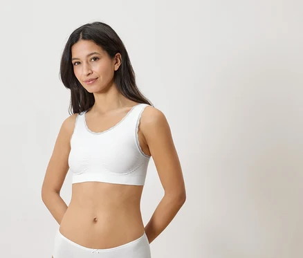 Une femme portant un soutien-gorge blanc bordé de dentelle et des sous-vêtements assortis sur un fond clair.